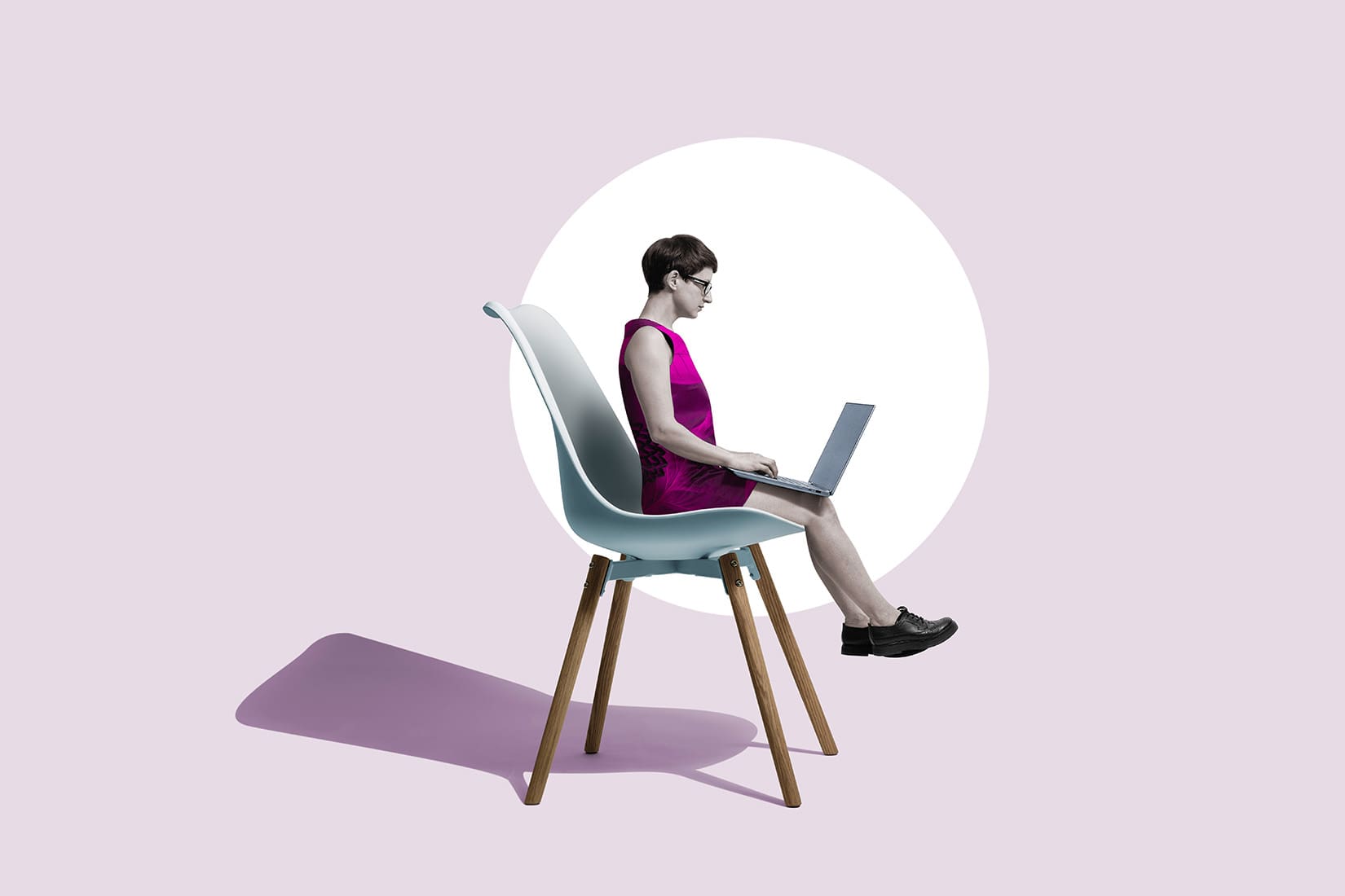 Side view of a woman sitting on an oversized office chair using a laptop, set against a solid pale purple background.